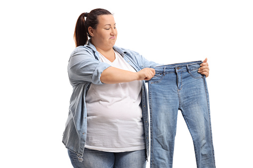 Sad overweight woman holding a pair of small jeans isolated on white background