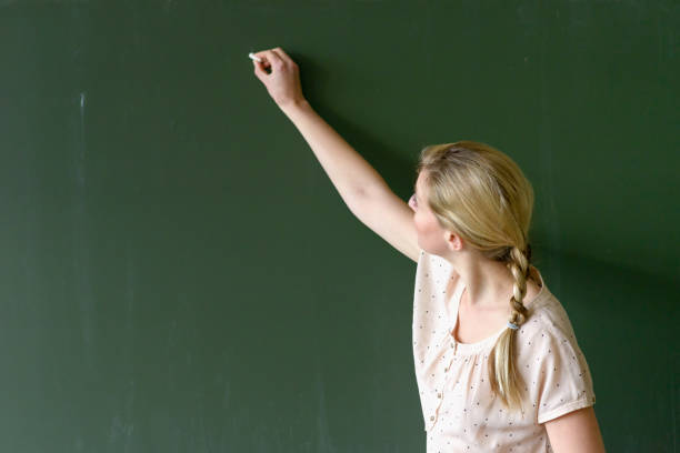 istock Female teacher writing with chalk on a chalkboard 1202464826