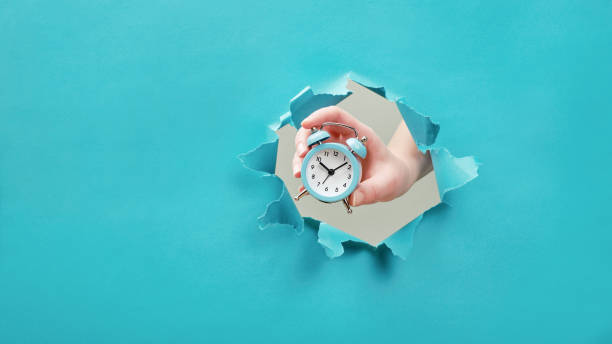 istock Hand holds alarm clock through a paper hole. Time management and deadline concept 1202466069