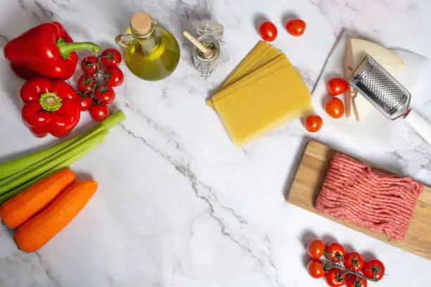 Photo of Raw ingredients for Italian meat lasagna. Top view of minced meat, pasta, tomatoes, olive oil, parmesan cheese, red paper, carrot celery for home cooking popular Italian dish