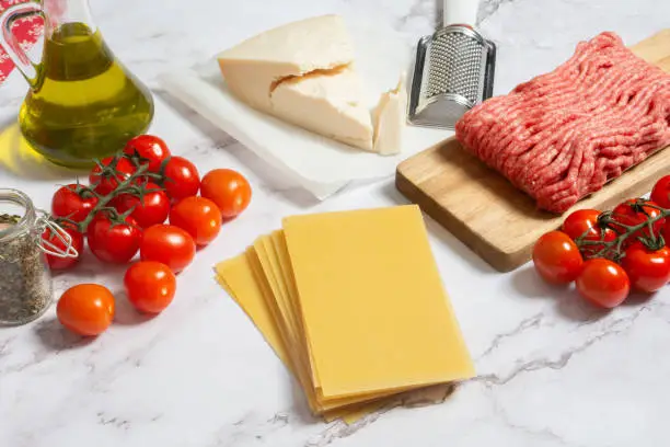 Photo of Raw lasagna sheets pasta with cherry tomatoes, parmesan cheese, minced meat and olive oil