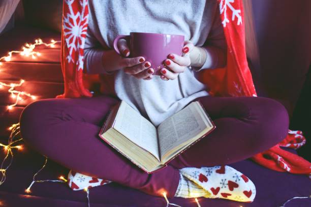 istock Woman indoora reading a book, holding a coffee mug 1202466410