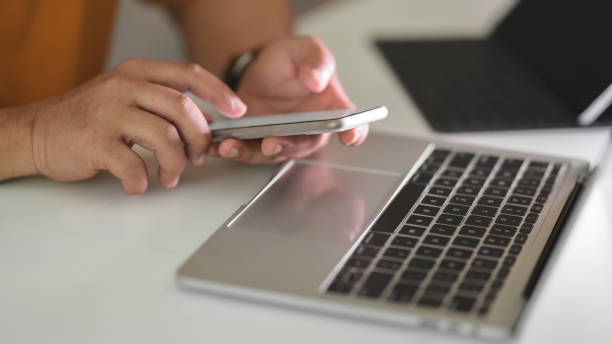 istock Side view of male freelancer typing on smartphone while working on laptop and tablet in workspace 1202467025