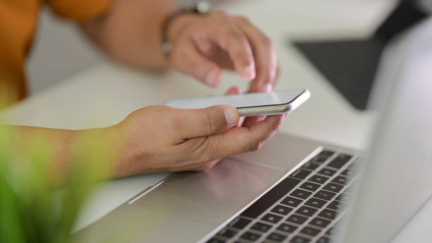 istock Side view of male freelancer typing on smartphone while working on laptop in office room 1202467090
