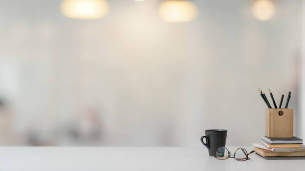 vista de cerca del espacio de trabajo con papelería, vasos y taza de café sobre mesa blanca con fondo borroso - escritorio fotografías e imágenes de stock