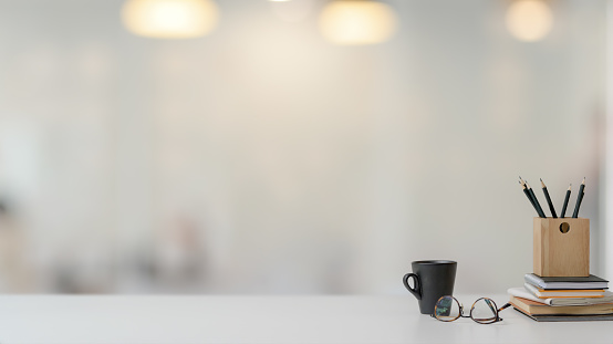 Close up view of simple workspace with copy space, stationery, glasses and coffee cup on white table with blurred background