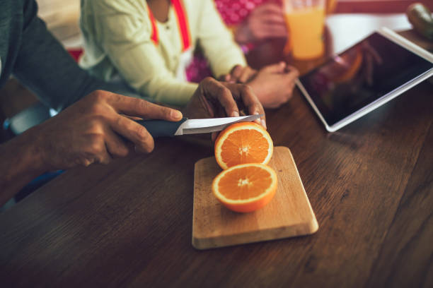 Hand slicing orange on wooden board.Black man in kitchen at home slicing fresh orange fruits on cutting board for salad or juicing.