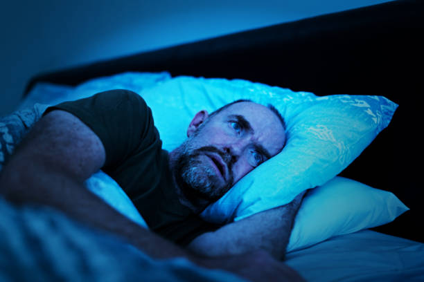 istock Depressed man lies in bed unable to sleep 1202469600