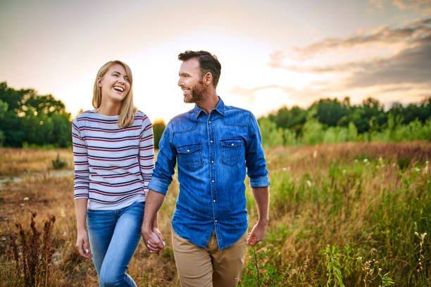 istock Smiling couple walking through meadow on sunny day and holding hands 1202473803