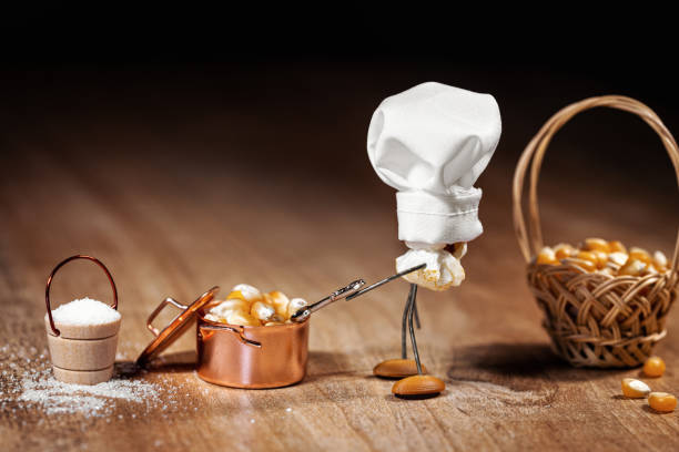 Funny scene with popcorn figures on a wooden table, black background, copper pot with popping maize or corn it