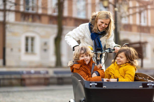 mother checking on her children who is riding in the front section of a cargo bike - cycling bicycle women city life imagens e fotografias de stock