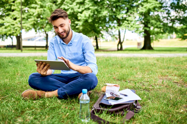 istock Handsome young man sitting on grass in park with tablet during lunch break 1202481714