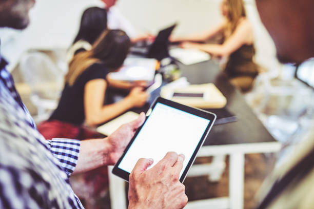 Closeup shot of two unrecognisable businessmen using a digital tablet in an office with their colleagues in the background