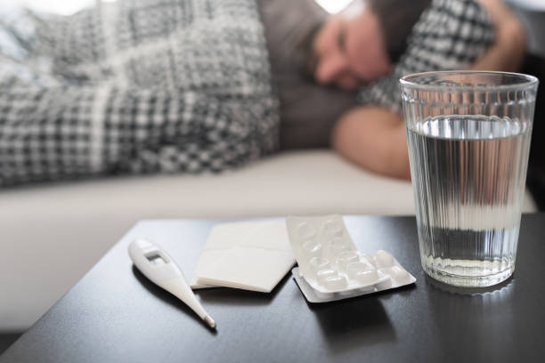 침대에서 자고있는 사람에 대한 야간 스탠드에 약, 의료 온도계 및 물 한 잔 - man flu 뉴스 사진 이미지
