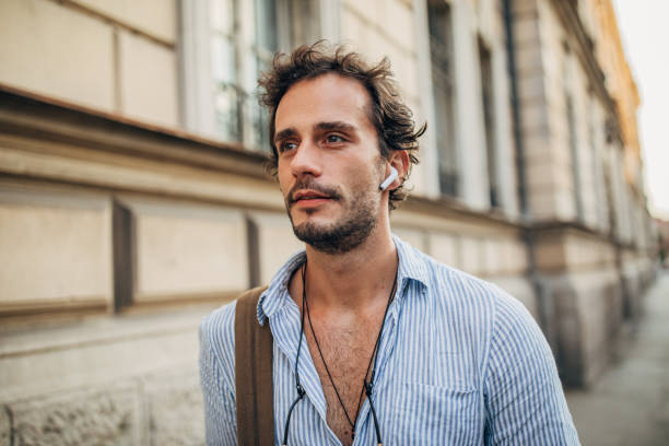 homme de hipster dans la ville écoutant la musique sur des écouteurs sans fil - men smiling headphones individuality photos et images de collection