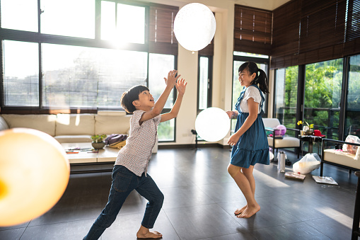 Taiwanese school aged brother and sister playing with balloons at home