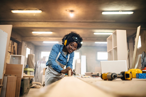 One African-American female carpenter working with wood in her workshop.