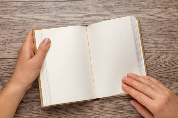 istock A5 open book mockup with hands. Empty template of page. Blank for design. On wooden background 1202486751