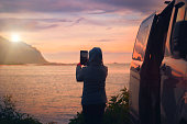 woman at the car photographs the sunset on the sea