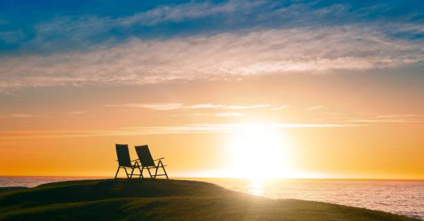 Two people sit in red beach chairs watching the waves crash against the rocks on an empty beach in Asbury Park, NJ in November.