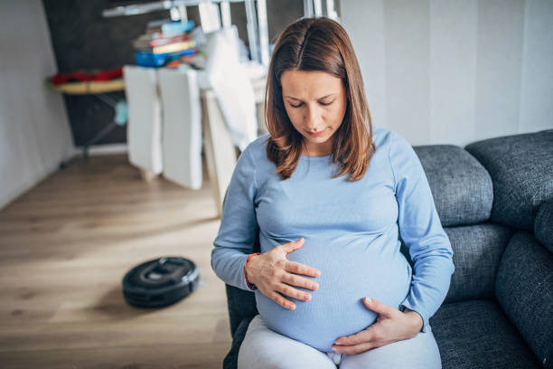 istock Pregnant woman resting while robot vacuum cleaner cleaning floor 1202492918