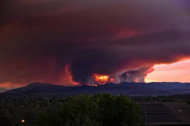 Photo of Fires out of control are spreading quickly in the Brindabella mountains. At night, the flames illuminate this huge dark cloud. The fires threaten suburbs in South Canberra. A massive cloud of smoke spreads over the city.