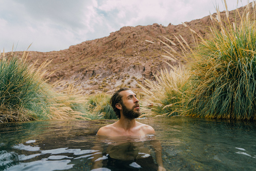 Young Caucasian man swimming  in hot spring in Atacama desert
