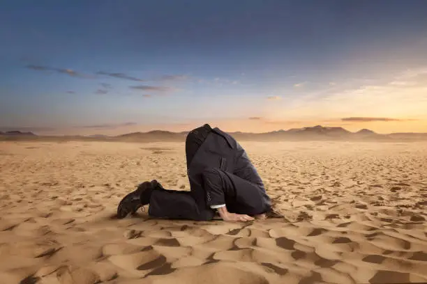 Desparate businessman hiding head in the sand at the desert with copy space