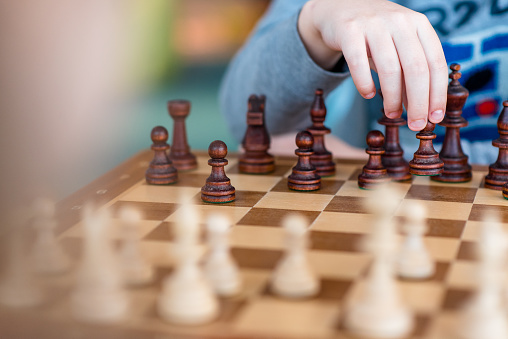 A child spending time playing chess. Chess figures close up with a moving hand.