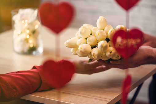 Valentines day.  Close-up of woman and man celebrating in restaurant. Boyfriend giving bouquet of flowers tulips to girlfriend. View through a heart-shaped garland. love, romance, date