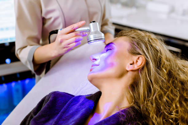 cosmetologia da pele. mulher esteticista fazendo terapia de luz azul no rosto de uma jovem loira bonita - galvanic - fotografias e filmes do acervo