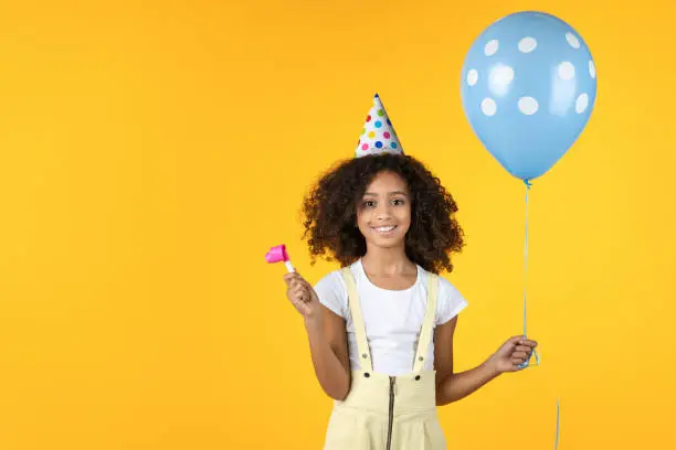 Photo of Cute little girl with party hat holding balloon isolated on yellow background