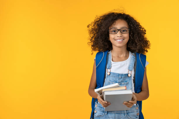 wesoła młoda afrykańska dziewczyna dziecko w okularach trzymających notatnik i książki do nauki odizolowane na żółtym tle - schoolgirl zdjęcia i obrazy z banku zdjęć
