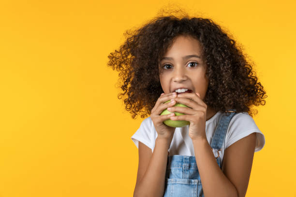 niña comiendo manzana sobre fondo amarillo - apple healthy eating eating black fotografías e imágenes de stock
