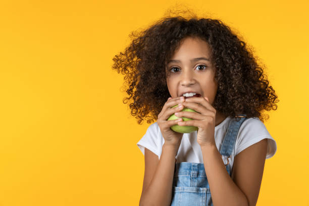 mała dziewczynka jedząca jabłko na żółtym tle - apple eating little girls green zdjęcia i obrazy z banku zdjęć