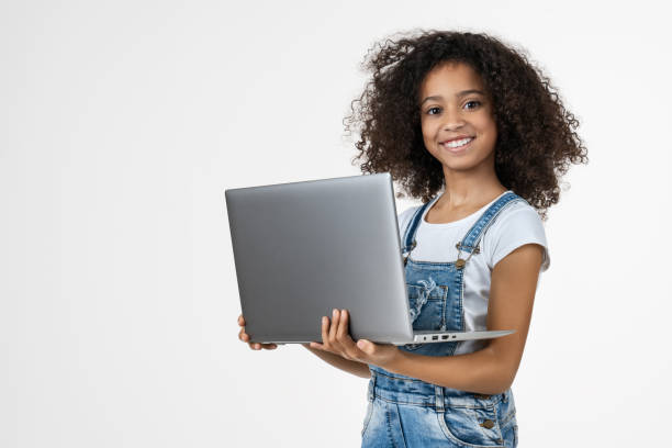 portrait of little girl holding laptop computer while standing and looking at camera isolated over white background - child computer laptop little girls imagens e fotografias de stock