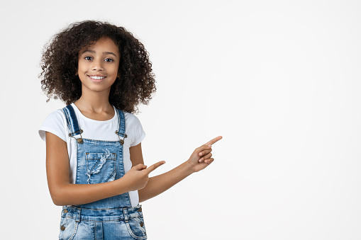 Happy african american girl pointing fingers aside at copy space isolated over white background