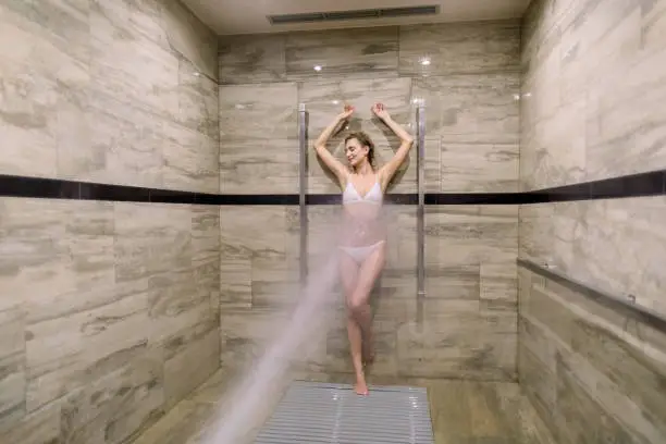 Young woman having high pressure shower after the treatment wrapping procedure at the modern spa salon. Concept of hydrotherapy and Sharko shower.