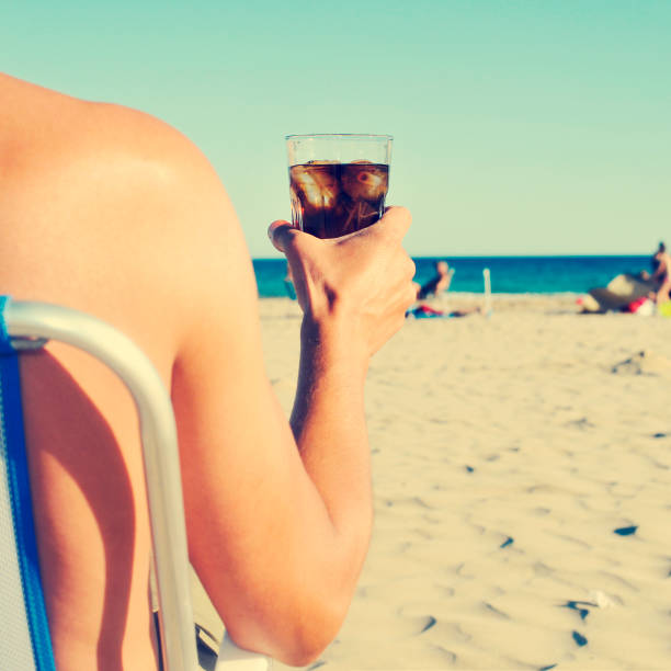 a young caucasian man hanging out on the beach with a glass with cola drink, with a filter effect