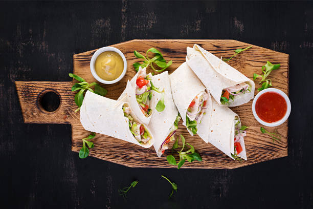 Fresh tortilla wraps with chicken and fresh vegetables on wooden board. Chicken burrito. Mexican food. Healthy food concept. Mexican cuisine.Top view, overhead