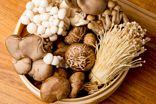 Assortment of mushrooms, portobello, chanterelles, hen of the woods, shiitake and button mushrooms shot in wooden basket on wooden cutting board.