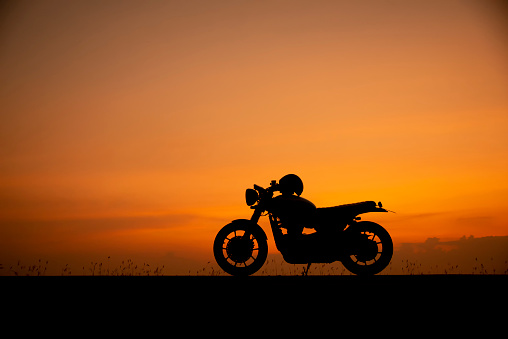 Silhouette of motorcycle parking with sunset background in Thailand,Young Traveller man placed helmet on motorbike.Trip and lifestyle of Motorcycle Concept.