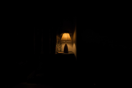 A lamp on a table next to a bed at night time
