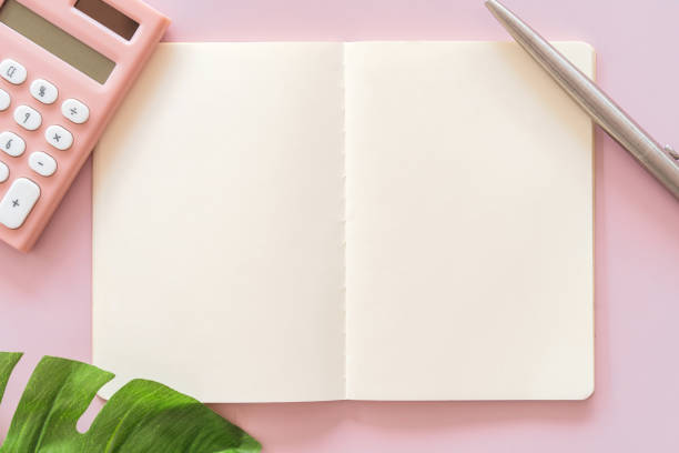 istock Copy space of note book with pen and calculator frame green leave on pink table background. 1202522393