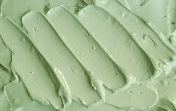 Photo of Green cosmetic clay (avocado facial mask, cucumber face cream, body wrap) texture close up, selective focus. Abstract background with brush strokes.