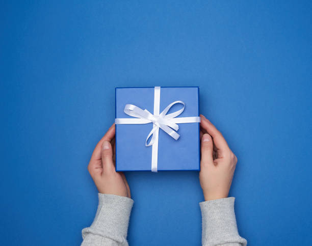 istock two female hands in a sweater hold a square blue box with a bow 1202524397
