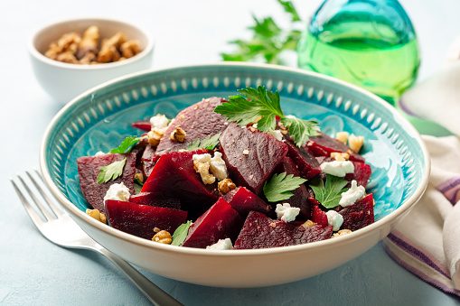Healthy beetroot salad with walnuts, feta cheese and parsley on blue concrete background. Selective focus.