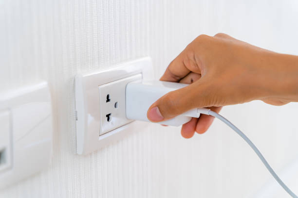 istock Woman's Hand Inserting Electrical Power Cord Plug into Receptacle on wall outlet. 1202530700