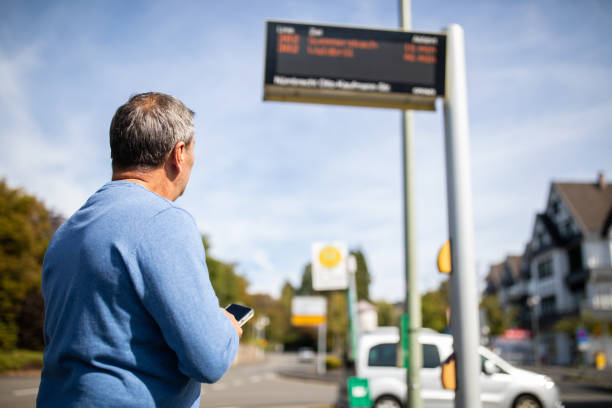 Mature man standing and looking at bus arrival information system for passengers while waiting for a bus