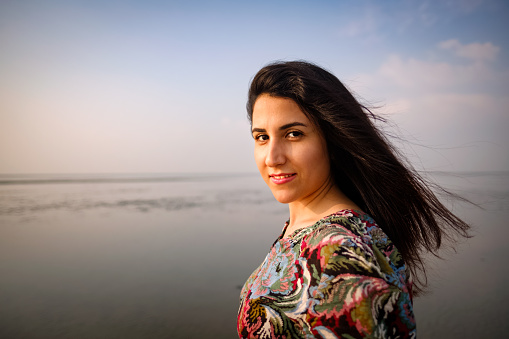 A portrait of smiling beautiful iranian persian girl outdoor on the beach looking at camera.
